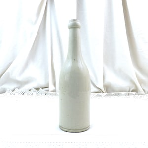 May include: A white ceramic bottle with a rounded bottom and a slightly flared neck. The bottle has a smooth, matte finish and is slightly textured.