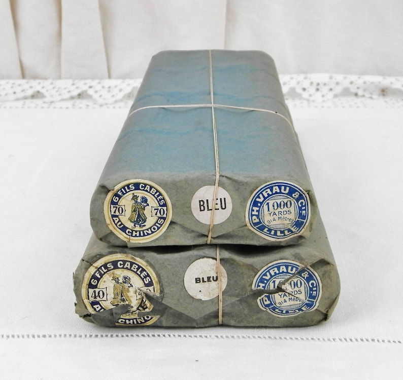 May include: Two bundles of blue thread wrapped in brown paper with labels that read "6 Fils Cables 70 Au Chinois" and "Ph. Vrau & Cie Lille 1000 Yards 914 Metres" and "Bleu".