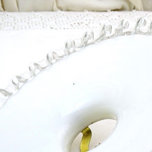 Puede incluir: Un plato de cer&aacute;mica blanco con un borde festoneado. El plato tiene un agujero en el centro y un dise&ntilde;o dorado alrededor del agujero.