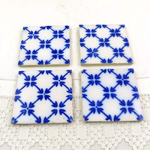 May include: Four square ceramic tiles with a white background and a blue arrow pattern. The tiles are arranged in a square formation, showcasing a repeating design. The tiles have a slightly aged appearance.