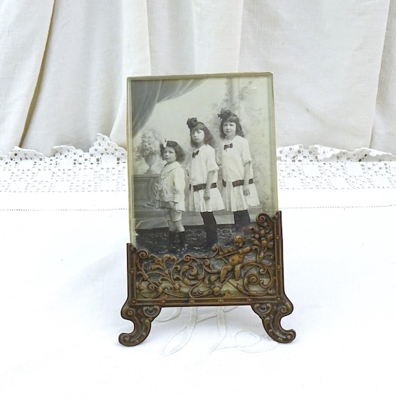 Antique French Free Standing Frame Decorated with a Cherub in Bronze Tone Embossed Metal and Black and White Photograph Sisters and Brother