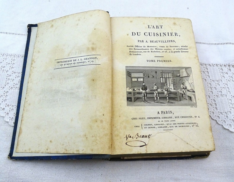May include: A vintage book titled "L'Art du Cuisinier" by A. Beauvilliers. The book is bound in blue and features a black and white illustration of a kitchen scene on the cover.