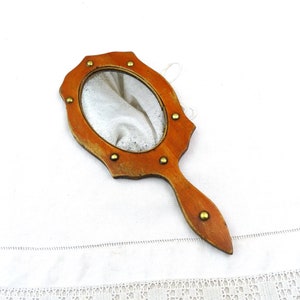Könnte beinhalten: Ein hölzerner Handspiegel mit braunem Rahmen und goldenen Akzenten. Der Spiegel hat eine runde Form und ist mit kleinen goldenen Nieten verziert.