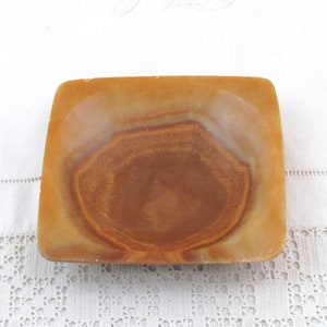 May include: A square, shallow dish made of brown and orange alabaster with a swirling pattern. The dish is empty and has a smooth, polished surface.