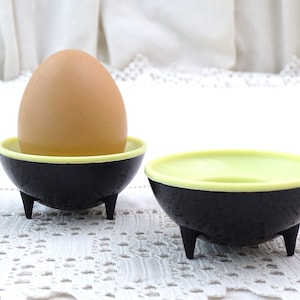 May include: Two black and lime green egg cups with three legs each. One egg cup has a brown egg inside.