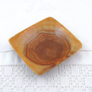 May include: A square, shallow dish made of brown and beige onyx with a swirling pattern. The dish is empty and sits on a white surface.