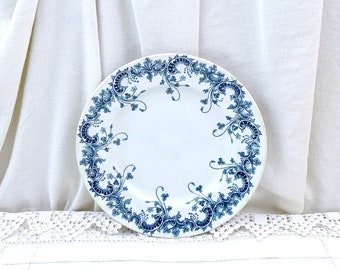 May include: A white ceramic plate with a blue and white floral design around the rim. The plate is on a white lace tablecloth.
