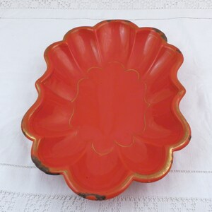 May include: A bright orange ceramic dish with a scalloped edge and a gold trim. The dish has a decorative design in the centre.