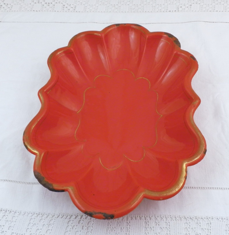 May include: A bright orange ceramic dish with a scalloped edge and a gold trim. The dish has a decorative design in the centre.