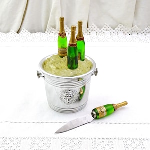 Peut inclure: Seau à champagne en argent avec trois bouteilles de champagne miniatures à l'intérieur et de la glace. Un couteau en argent avec un manche de bouteille de champagne vert et or.