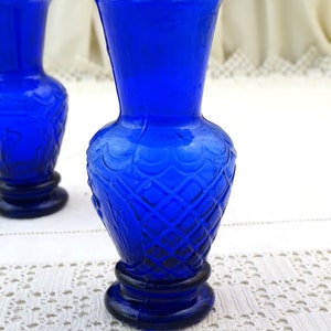 May include: Two cobalt blue glass vases with a diamond pattern and scalloped rims. The vases are on a white crocheted surface.