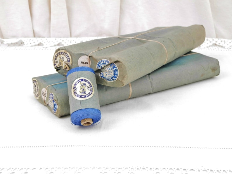 May include: A spool of blue thread wrapped in paper with labels that read "Fils Carres Au Chinois" and "100 Yards 91.44 m".