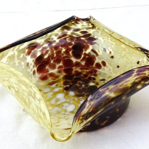 May include: A square-shaped glass bowl with a mottled brown and yellow pattern. The bowl has a unique, wavy design and a slightly flared rim.