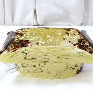 May include: A yellow glass bowl with brown speckles and a wavy rim. The bowl is square shaped with rounded corners.