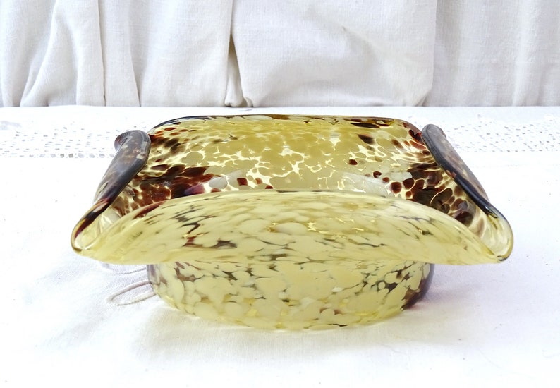 May include: A yellow glass bowl with brown speckles and a wavy rim. The bowl is square shaped with rounded corners.