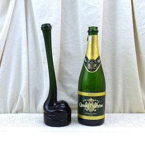 May include: A green glass bottle stopper shaped like a bird's head, next to a green glass bottle of Canard-Duchêne Brut Champagne.