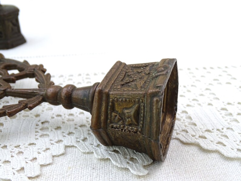 May include: A pair of antique brass candle holders with ornate designs. The holders are in the shape of a cross with a floral motif.