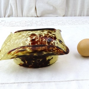 May include: A square-shaped glass bowl with a mottled brown and yellow pattern. The bowl has a unique, wavy design and is shown next to a brown egg.