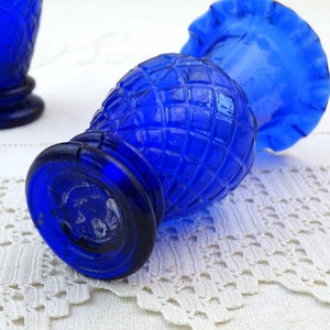 May include: Two cobalt blue glass bud vases with a diamond pattern and ruffled tops. The vases are sitting on a white crocheted surface.