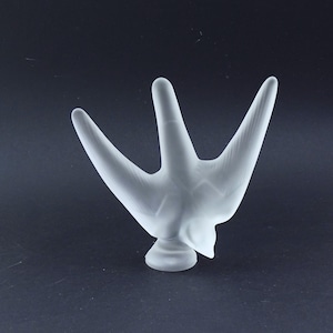May include: A frosted glass sculpture of a bird with a long, pointed beak and outstretched wings. The sculpture is white and has a smooth, polished finish.