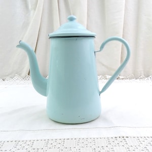 Puede incluir: Una cafetera vintage de esmalte azul claro con un pico curvo y un asa en forma de corazón. La cafetera tiene una tapa y un borde negro alrededor de la parte superior. Un artículo de cocina clásico.