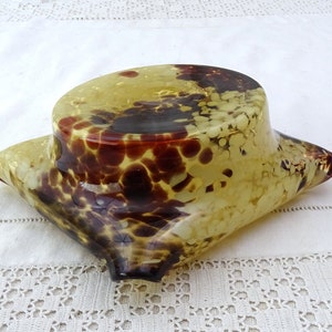 May include: A yellow glass bowl with brown and white speckles. The bowl is shaped like a pillow and has a rounded top.