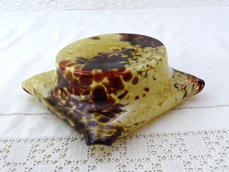 May include: A yellow glass bowl with brown and white speckles. The bowl is shaped like a pillow and has a rounded top.