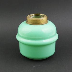 May include: A vintage, light green glass oil lamp reservoir with a brass collar. The rounded body has a ribbed design and a threaded brass top. The lamp is designed to hold oil for illumination.