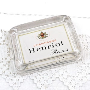 Puede incluir: Un cenicero de vidrio transparente con una etiqueta vintage que dice "Champagne Henriot Reims".