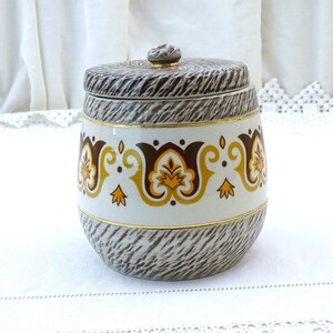 Puede incluir: Un tarro de cerámica con un patrón de veta de madera marrón y blanco y un borde dorado. El tarro tiene una tapa y está decorado con una banda de diseños florales marrones, amarillos y dorados.