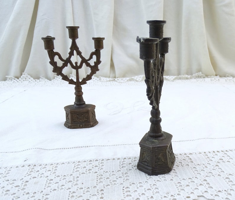 May include: Two ornate metal candle holders with a traditional design. The candle holders are made of a dark metal and have a detailed, intricate design.
