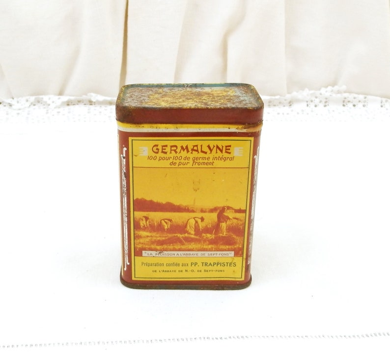 Puede incluir: Una lata rectangular y vintage de Germalyne con una etiqueta roja y amarilla. La etiqueta presenta el texto "GERMALYNE" y "100 pour 100 de germe int&eacute;gral de pur Froment". La lata tiene un aspecto r&uacute;stico y envejecido.