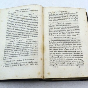 May include: An open book with yellowed pages and a blue cover. The book is titled "L'Art du Cuisinier" and contains text about cooking truffles and ragouts. The text is in French.