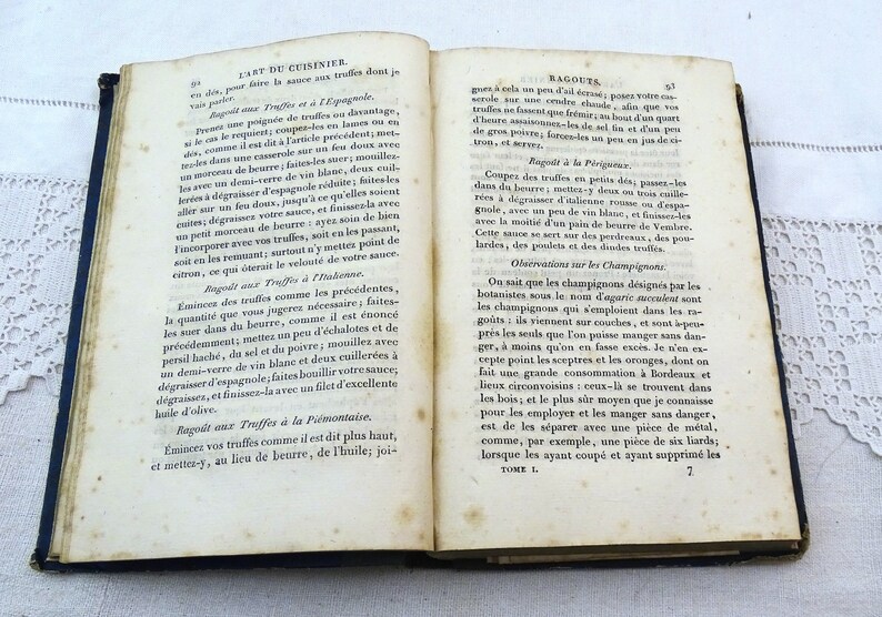 May include: An open book with yellowed pages and a blue cover. The book is titled "L'Art du Cuisinier" and contains text about cooking truffles and ragouts. The text is in French.