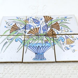 May include: Six white ceramic tiles featuring a hand-painted design of a blue vase with a bouquet of flowers. The flowers are brown, blue, and yellow.