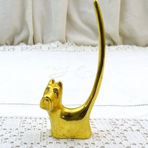 May include: Gold-colored ring holder shaped like a dog with rhinestone eyes. The dog is sitting up with its tail curled around its back.