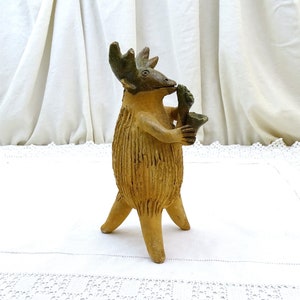 Könnte beinhalten: Eine Keramikfigur eines Elchs, der Saxophon spielt. Der Elch ist braun und hat ein grünes Saxophon. Die Figur steht auf einer weißen Oberfläche.