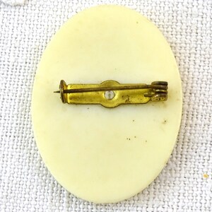 May include: The back of a white round pin with a gold metal pin back.