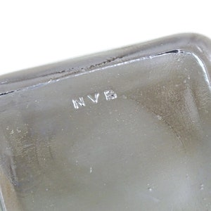 May include: Close-up of a clear glass container with the letters "NVB" etched into the bottom.