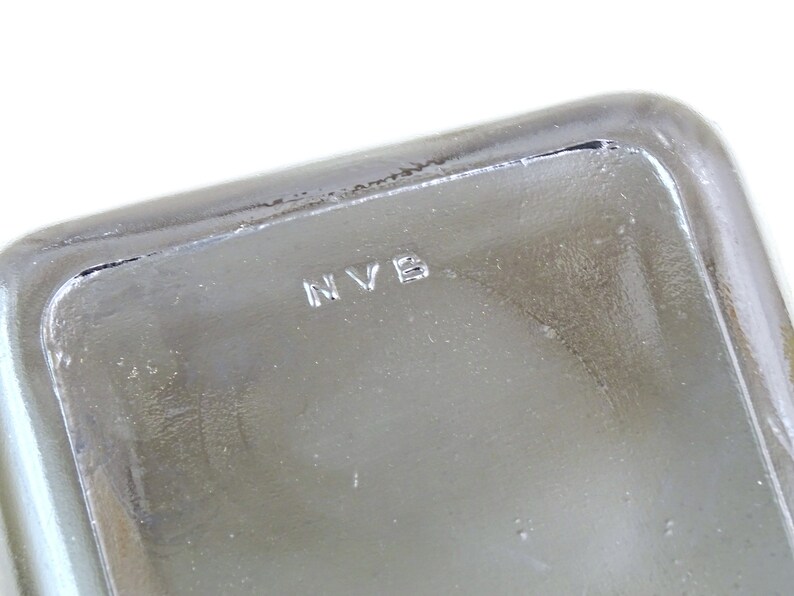 May include: Close-up of a clear glass container with the letters "NVB" etched into the bottom.