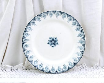 May include: White ceramic plate with a blue floral design around the rim and a starburst pattern in the center. The plate has a scalloped edge and a vintage aesthetic. The plate is likely for serving food.