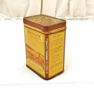 Puede incluir: Lata rectangular vintage de Germalyne con una etiqueta roja y amarilla. La etiqueta presenta texto y una ilustraci&oacute;n de personas en un campo. La lata tiene un aspecto oxidado y envejecido.
