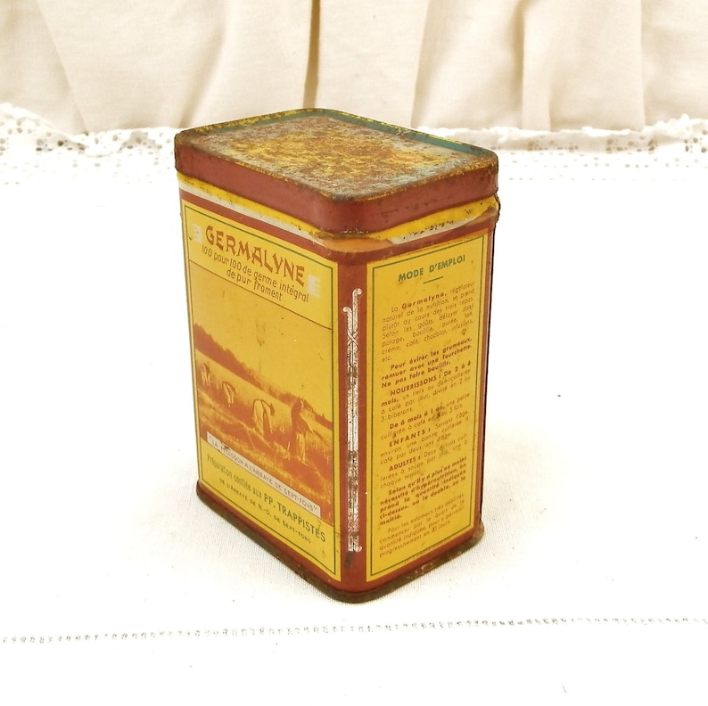 Puede incluir: Lata rectangular vintage de Germalyne con una etiqueta roja y amarilla. La etiqueta presenta texto y una ilustraci&oacute;n de personas en un campo. La lata tiene un aspecto oxidado y envejecido.