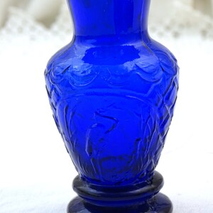 May include: A cobalt blue glass vase with a textured design. The vase has a round base and a narrow neck.