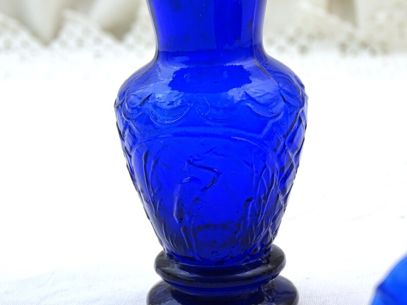 May include: A cobalt blue glass vase with a textured design. The vase has a round base and a narrow neck.