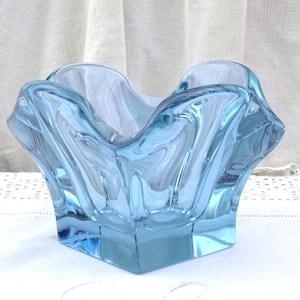 May include: A light blue glass bowl with a wavy, organic design. The bowl has a square base and is made of clear glass with a light blue tint.