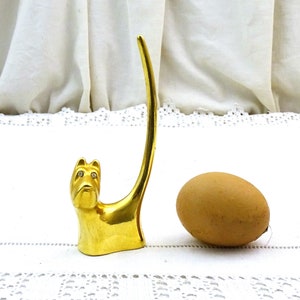 May include: Gold-tone ring holder shaped like a dog with rhinestone eyes. The dog's tail is curled up to form a ring holder.