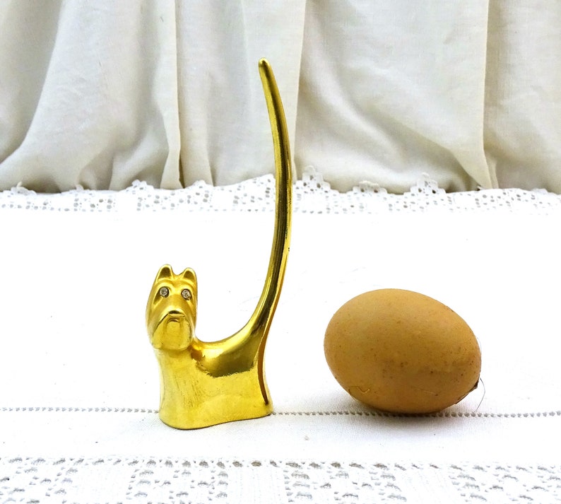 May include: Gold-tone ring holder shaped like a dog with rhinestone eyes. The dog's tail is curled up to form a ring holder.