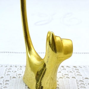 May include: Gold metal ring holder shaped like a cat. The cat is sitting up with its tail curled around to form a ring holder.
