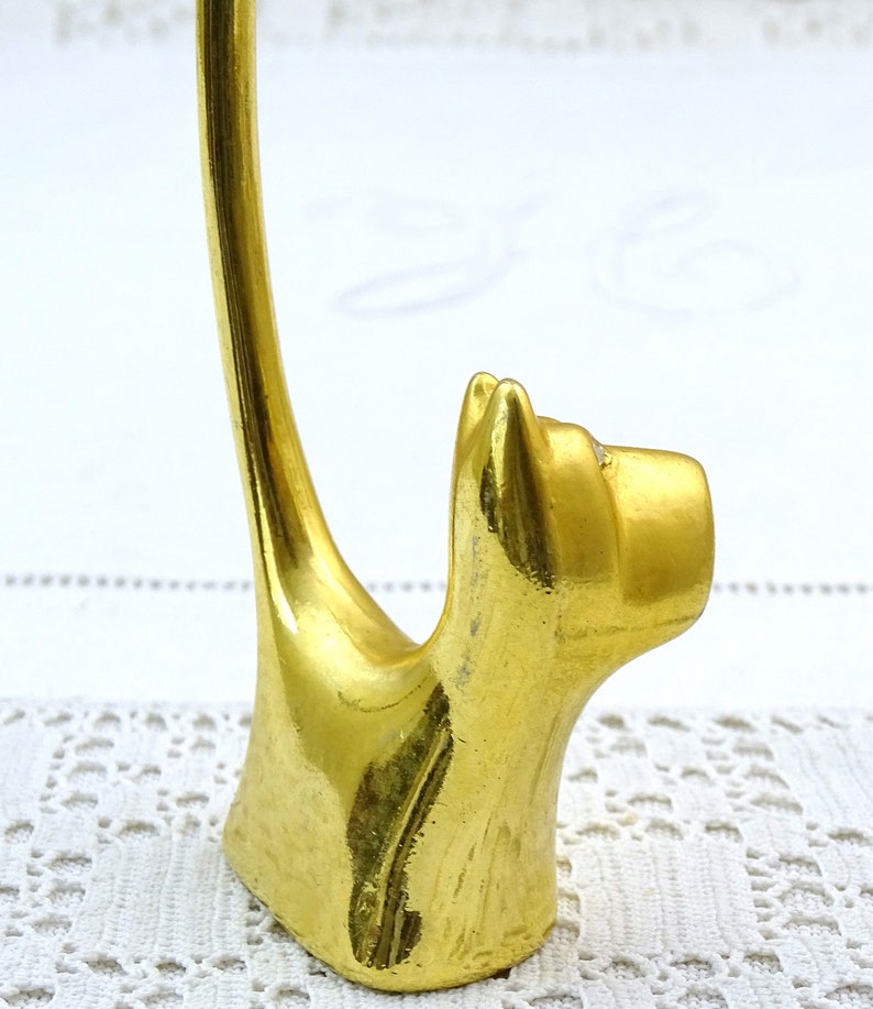 May include: Gold metal ring holder shaped like a cat. The cat is sitting up with its tail curled around to form a ring holder.
